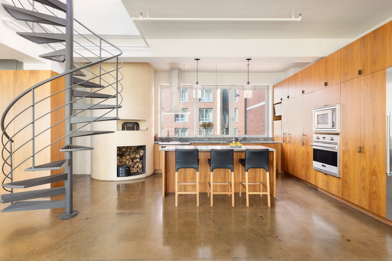 Penthouse kitchen with wood cabinetry, island seating, spiral staircase, and built-in fireplace.