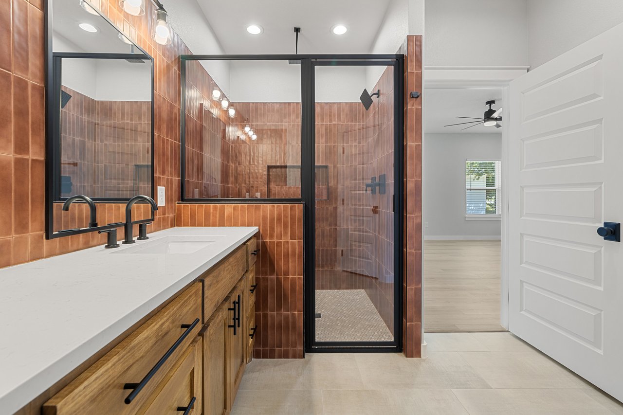 Modern bathroom with copper tile, black-framed glass shower, and wood double-sink vanity.