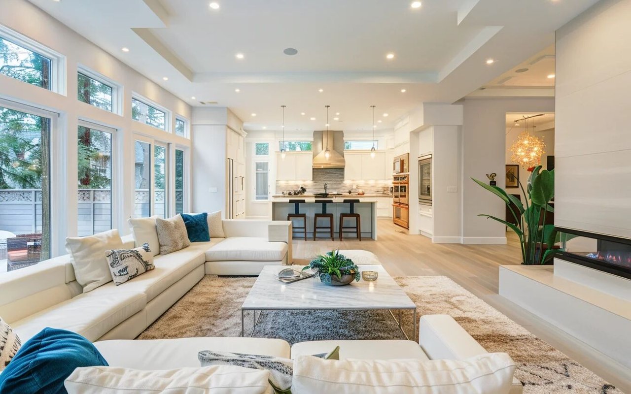 Open-plan living room with a white sectional, tall windows, fireplace, and kitchen island.