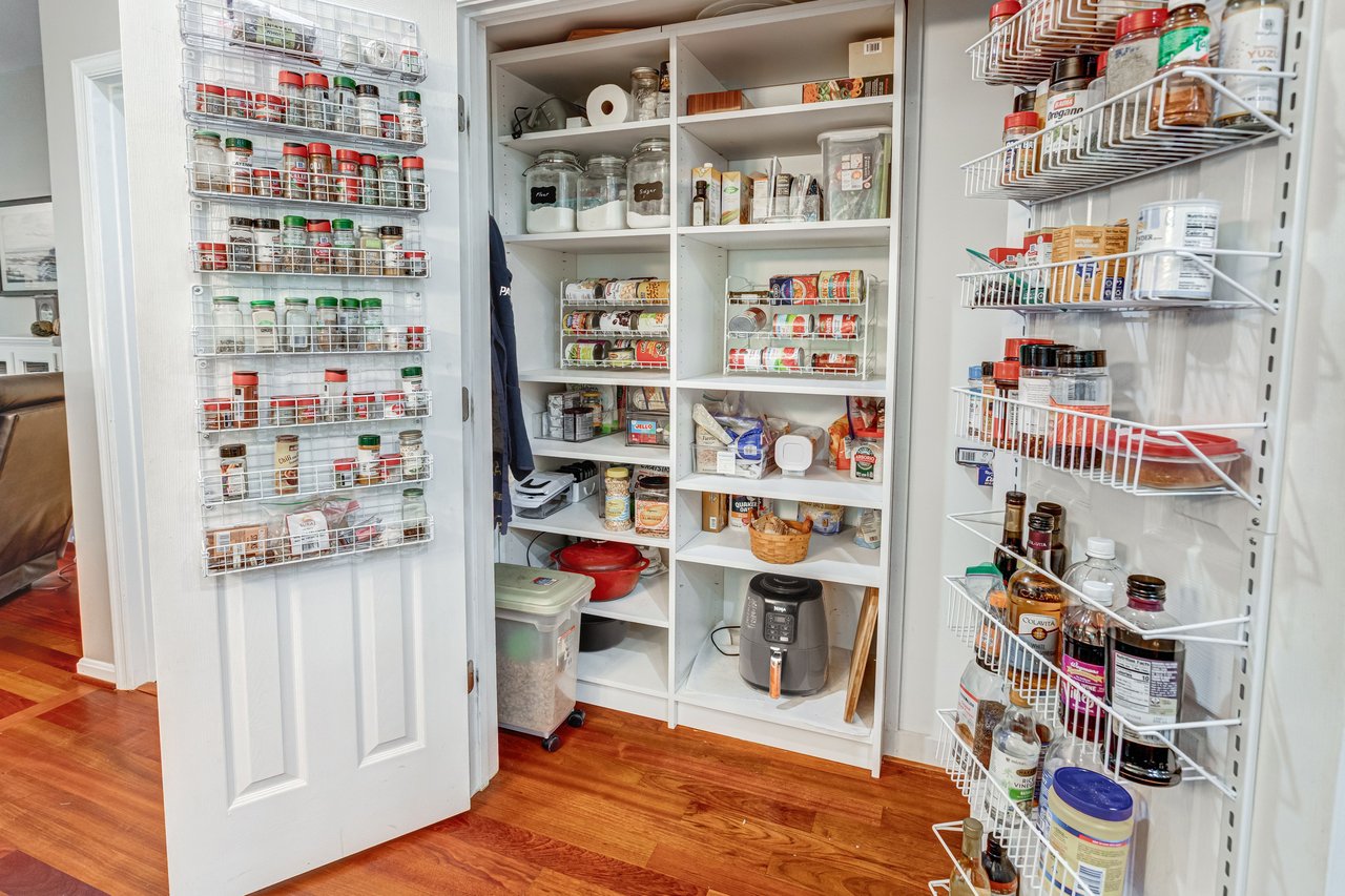 Walk-in pantry with stocked white shelves, wire door racks, and hardwood flooring.