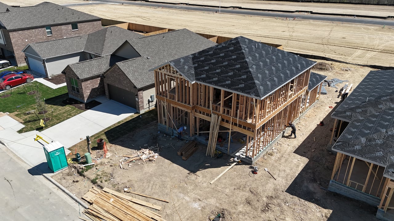 Aerial view of a wood-framed two-story home under construction beside finished houses.