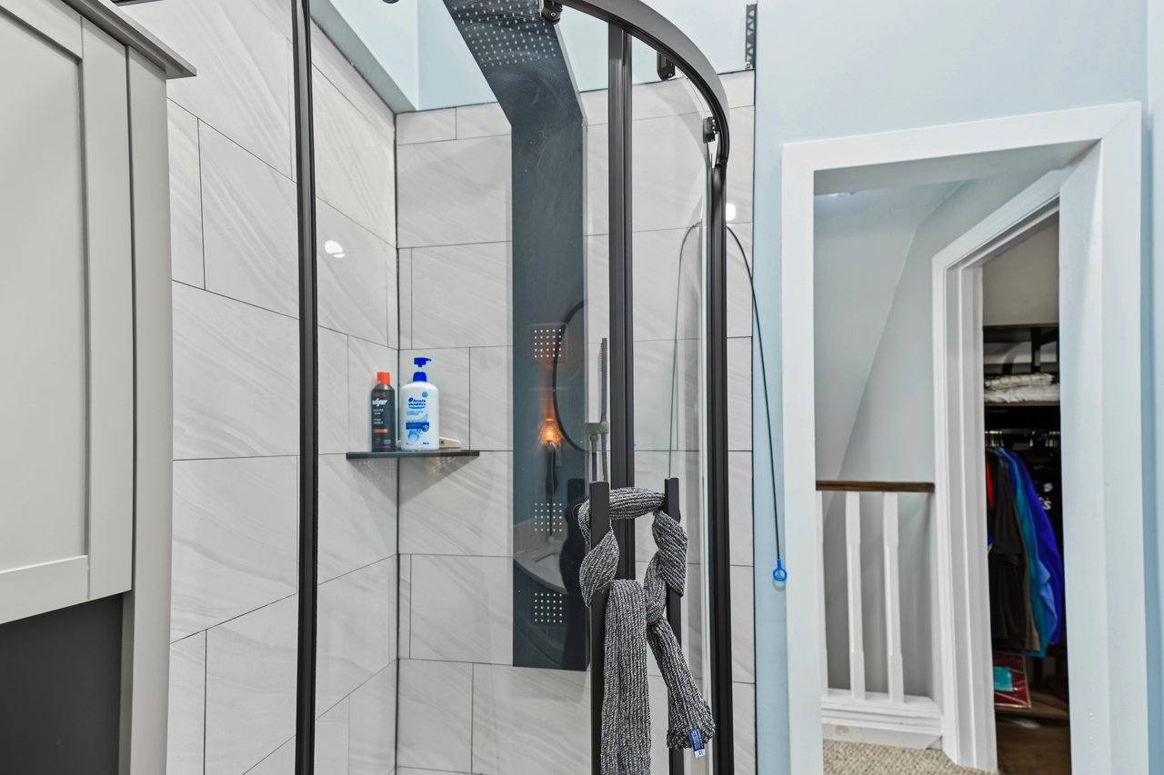 Bathroom shower with gray tile and dark shower panel beside an open closet.