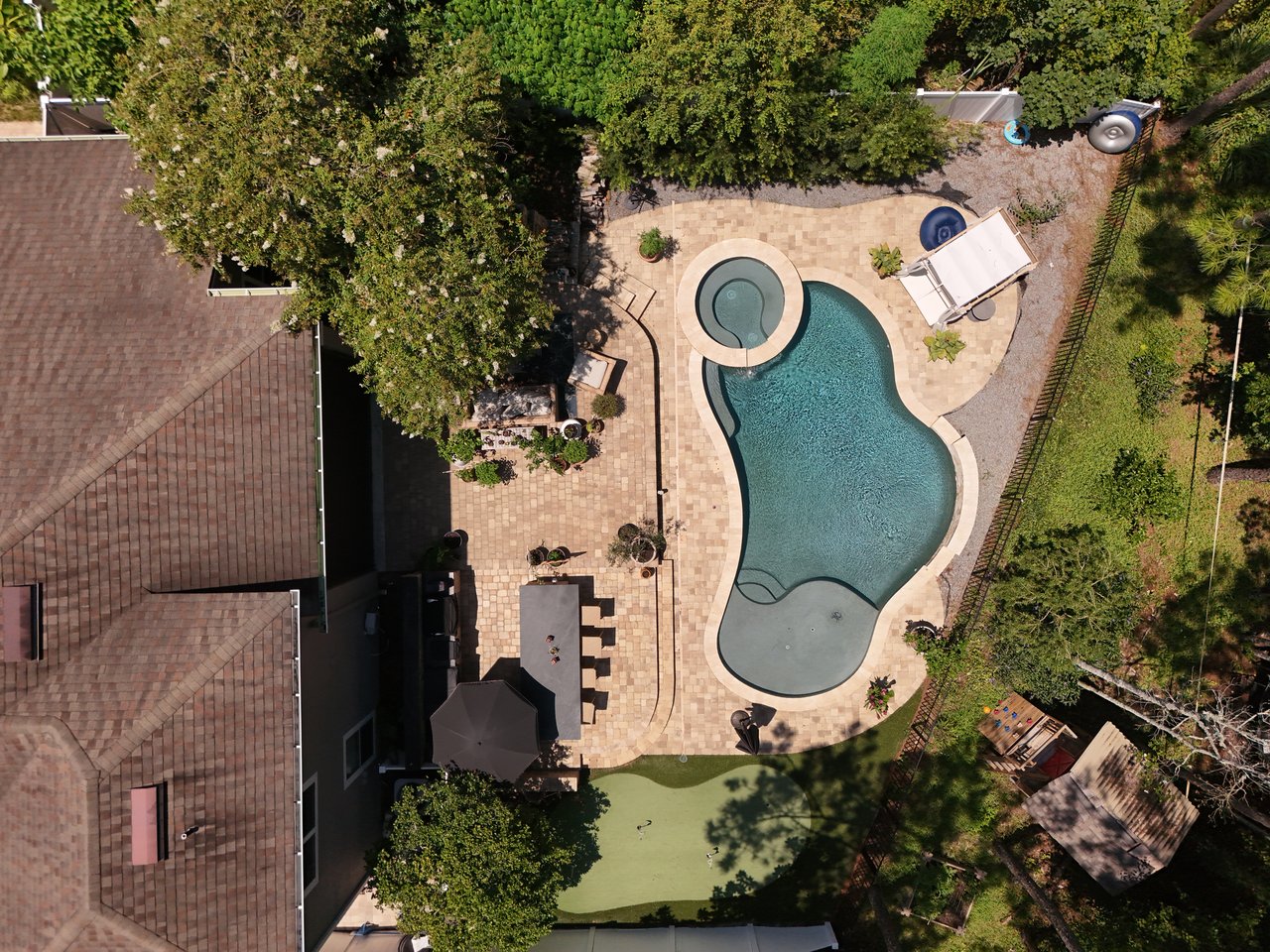 Aerial view of a backyard pool and circular spa beside a large paver patio.