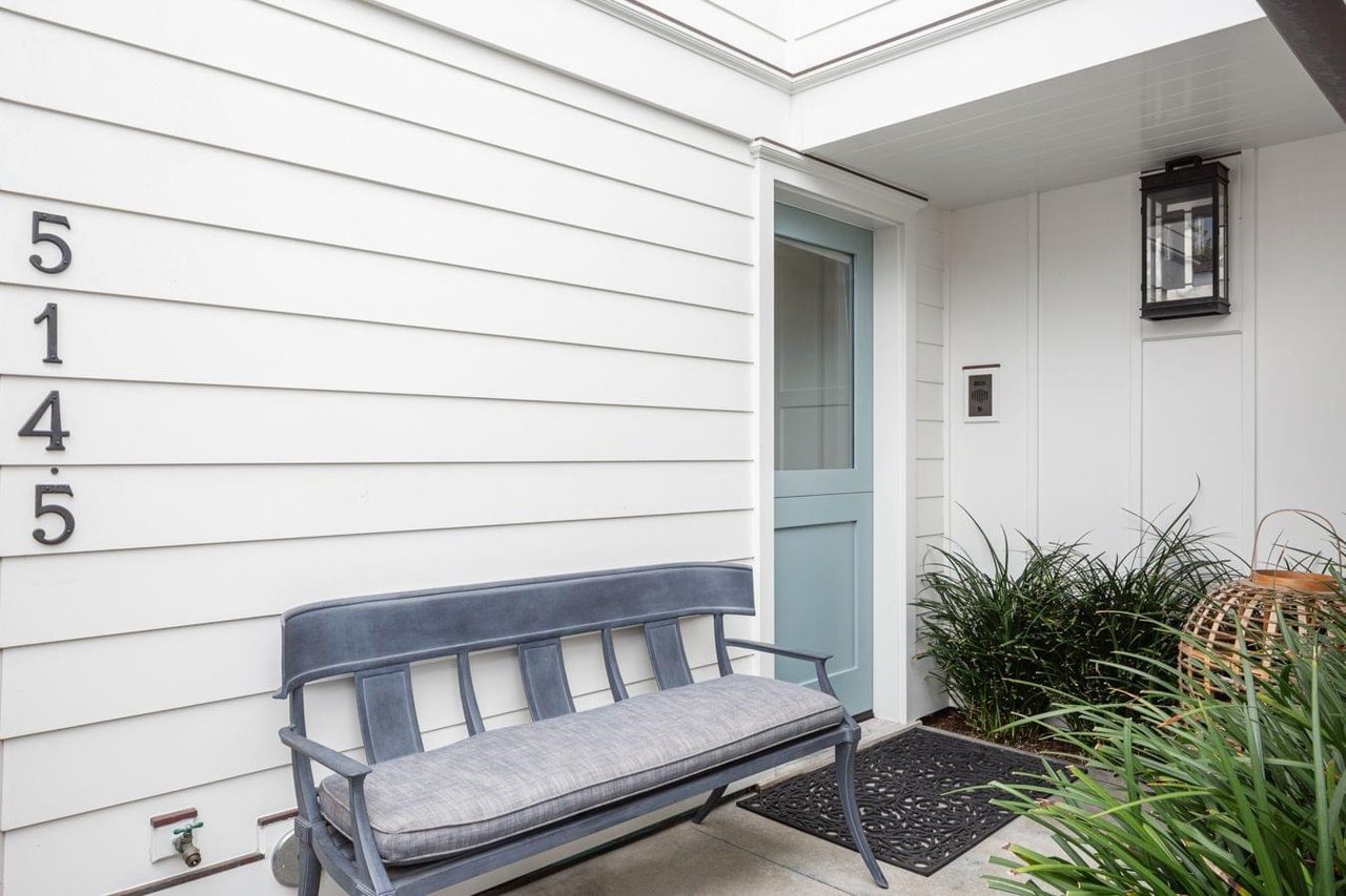 A close-up of a house's front porch, showing a blue dutch door, a dark blue bench, and the address numbers 5145.