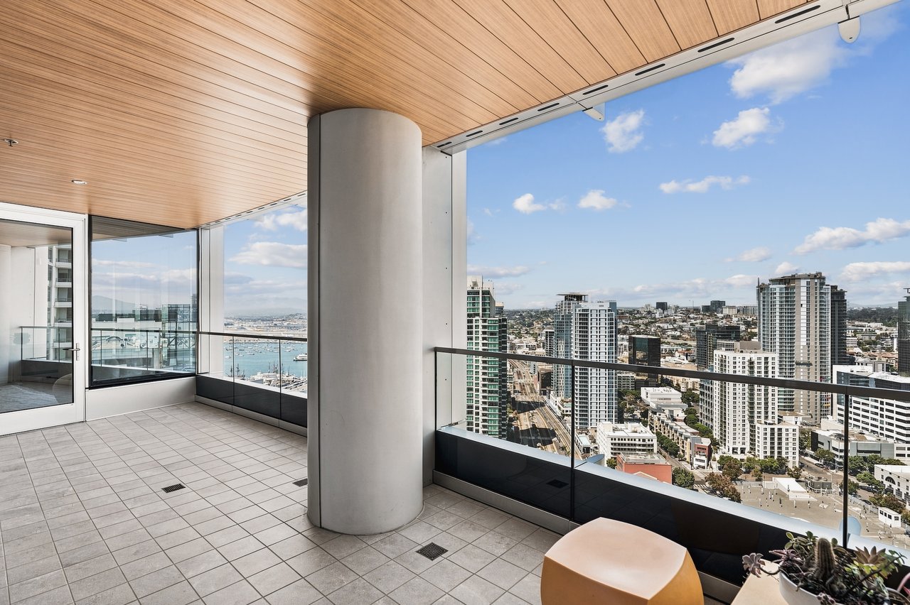 High-rise condo balcony overlooking downtown San Diego and the waterfront, with glass railings and a wood-paneled ceiling.