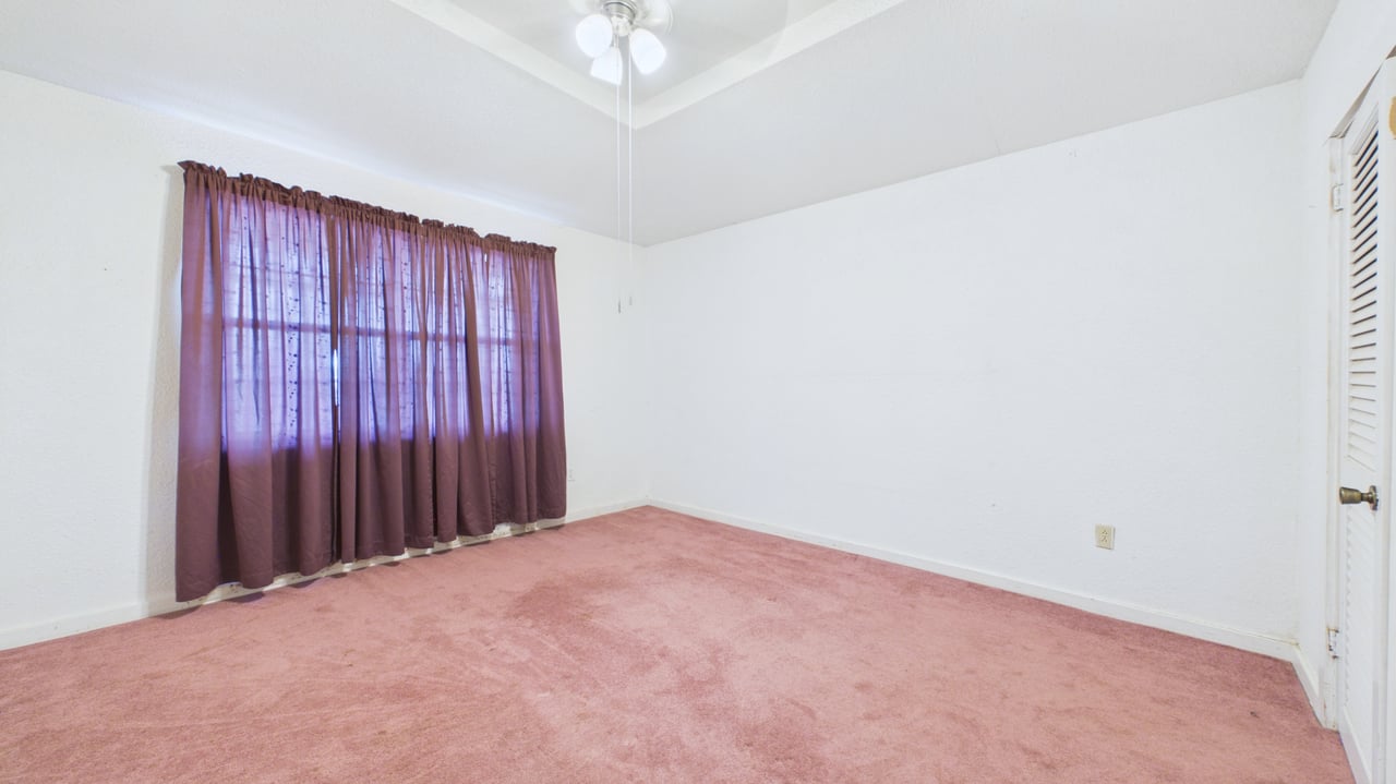Empty bedroom with pink carpet, purple curtains, and a ceiling fan.