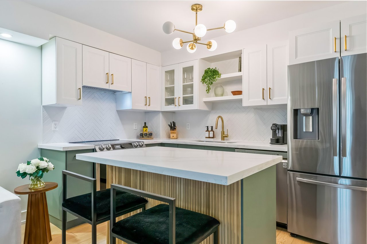 Modern white kitchen with a large island, gold accents, and stainless steel appliances.