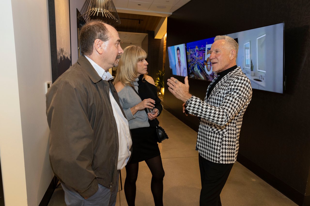 Three guests converse beside large property displays at an open house.