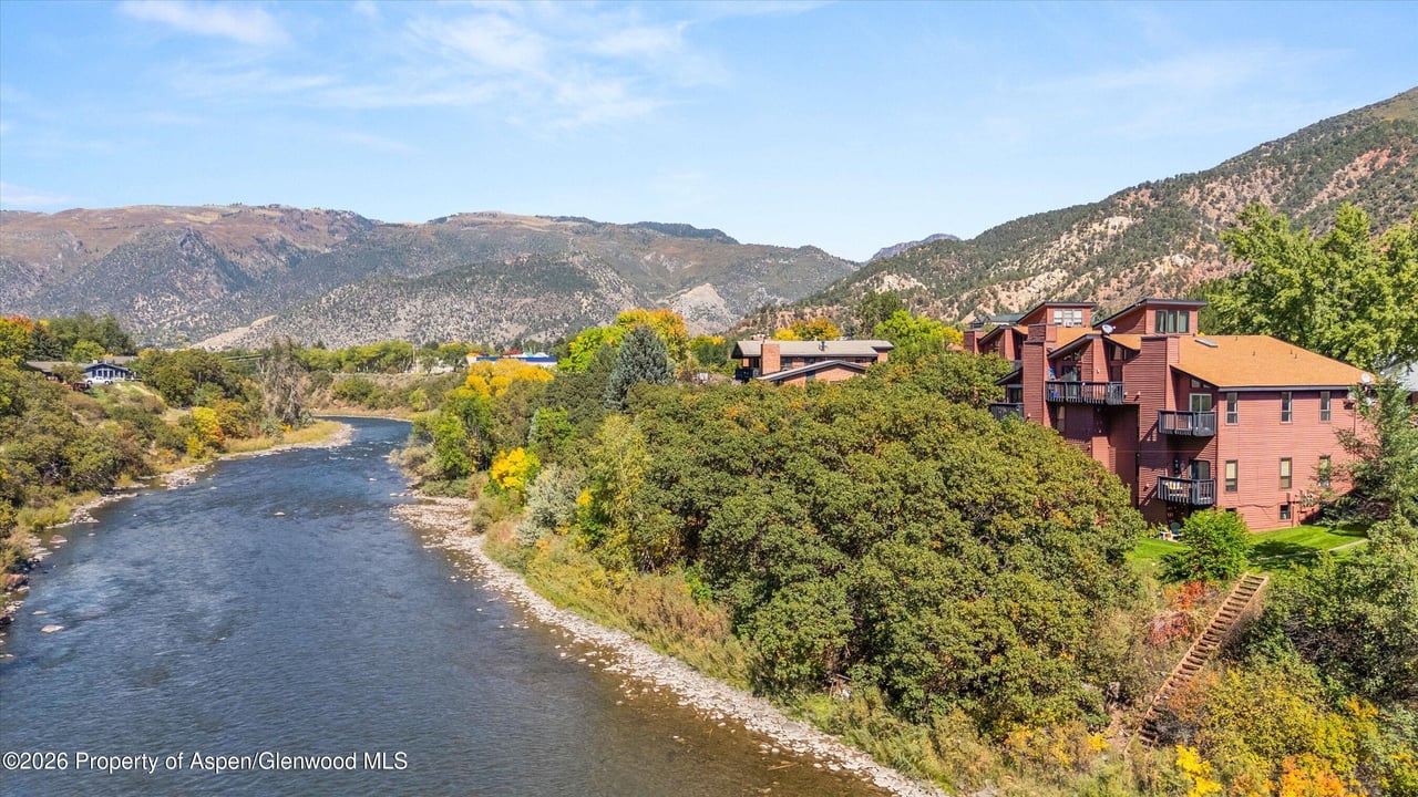 Red condominiums beside a river, with autumn foliage and mountains behind them.