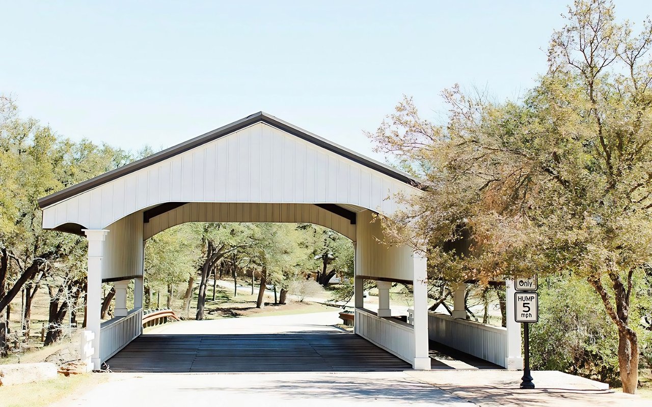 Covered wooden bridge with a white gabled roof and a low-clearance road sign.