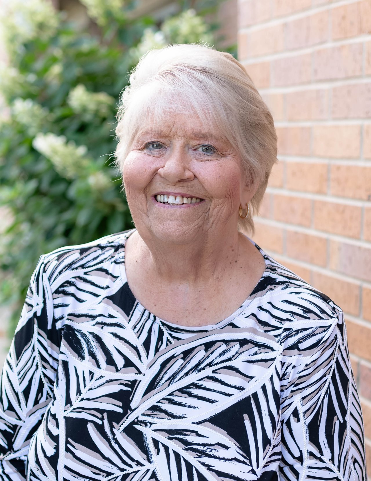 Dottie Moseley smiles outdoors beside a brick wall, wearing a black-and-white patterned top.