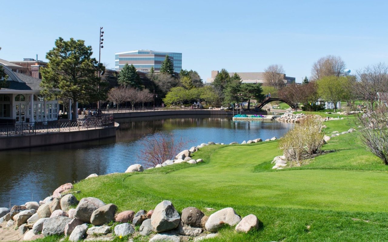 Landscaped city park with a pond, stone-lined banks, and a pedestrian bridge.