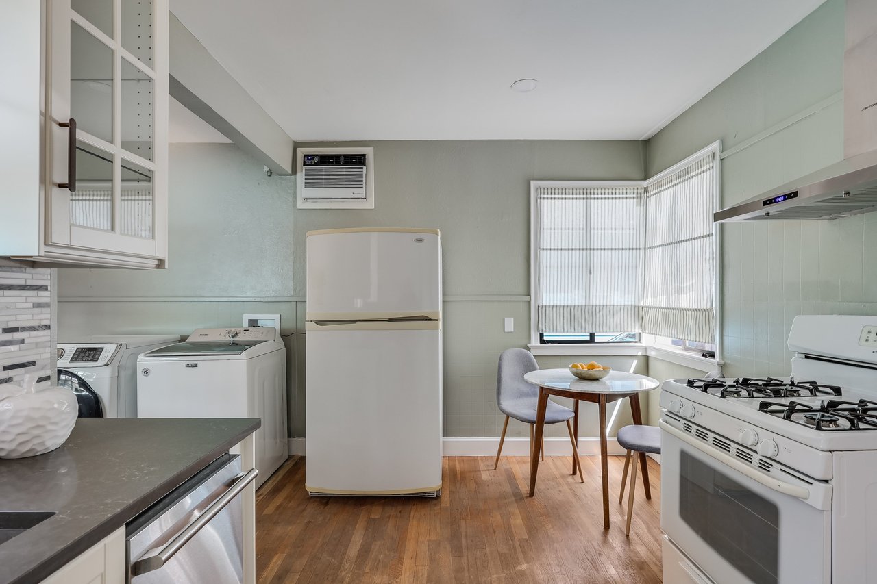 Kitchen with pale green walls, wood floors, and a small dining table beside a bay window.