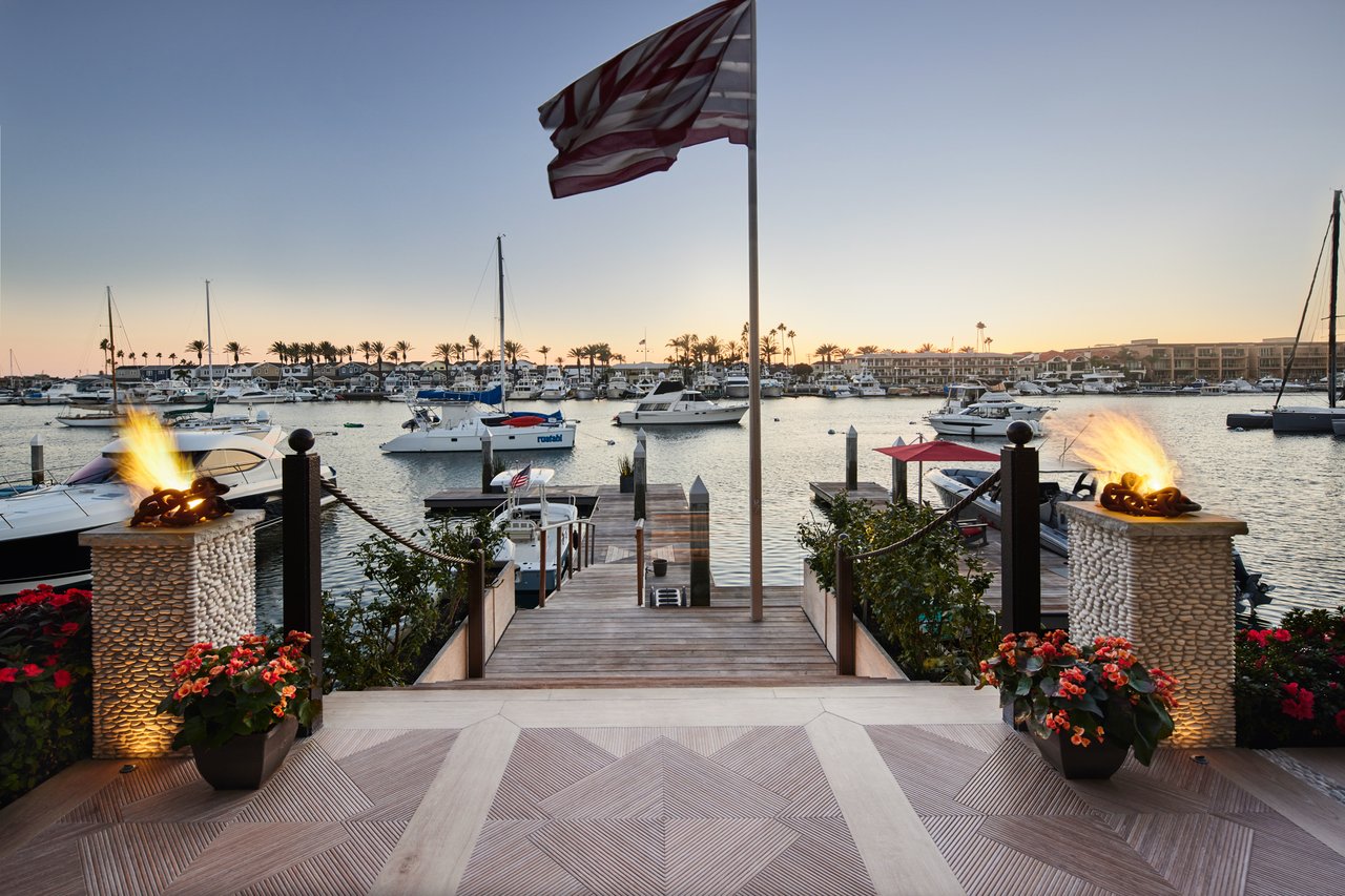 Waterfront patio overlooking a marina, framed by glowing fire features and flower planters.