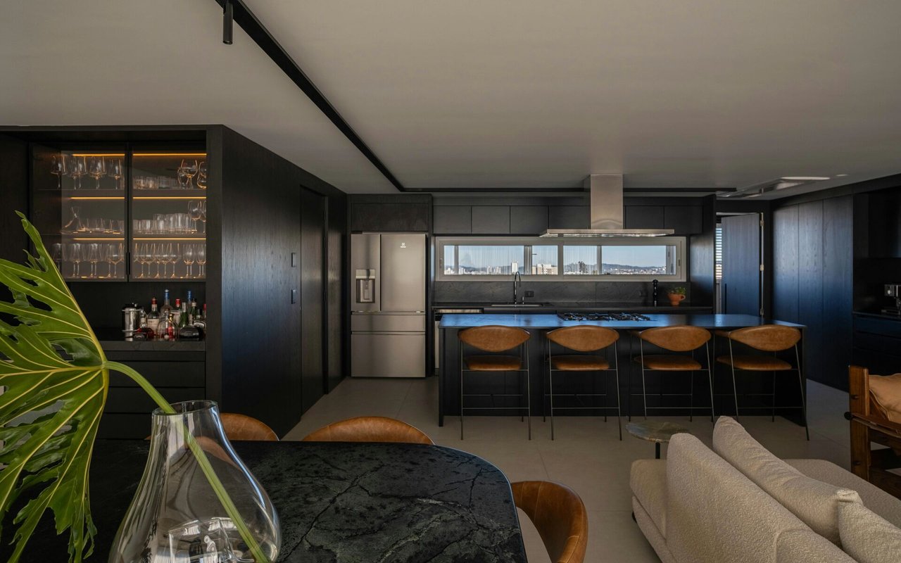 Modern dark kitchen with a four-seat island, glass-front bar cabinet, and city skyline view.