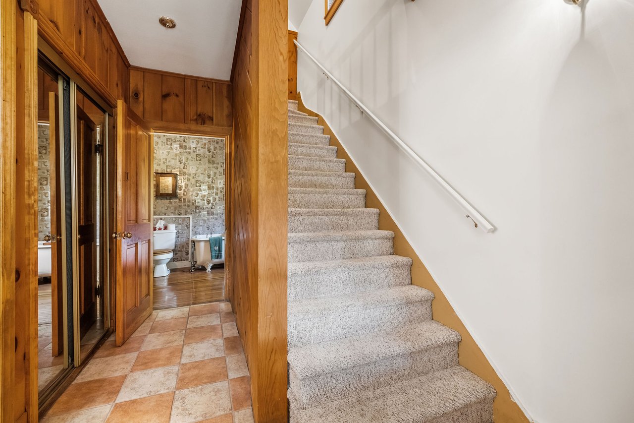 Carpeted staircase beside a wood-paneled hallway with tiled flooring and an open bathroom doorway.