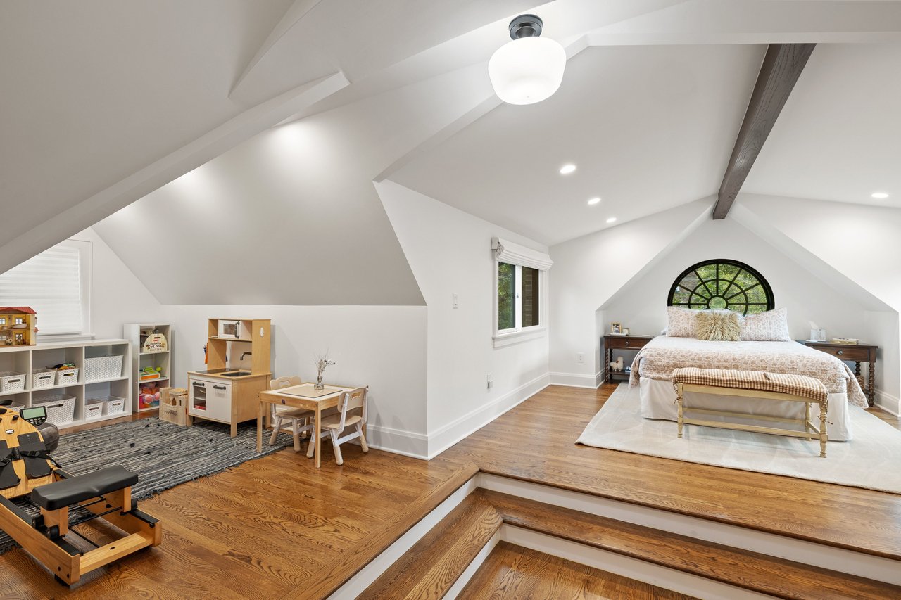 Attic bedroom with a bed beneath an arched window and a children’s play area