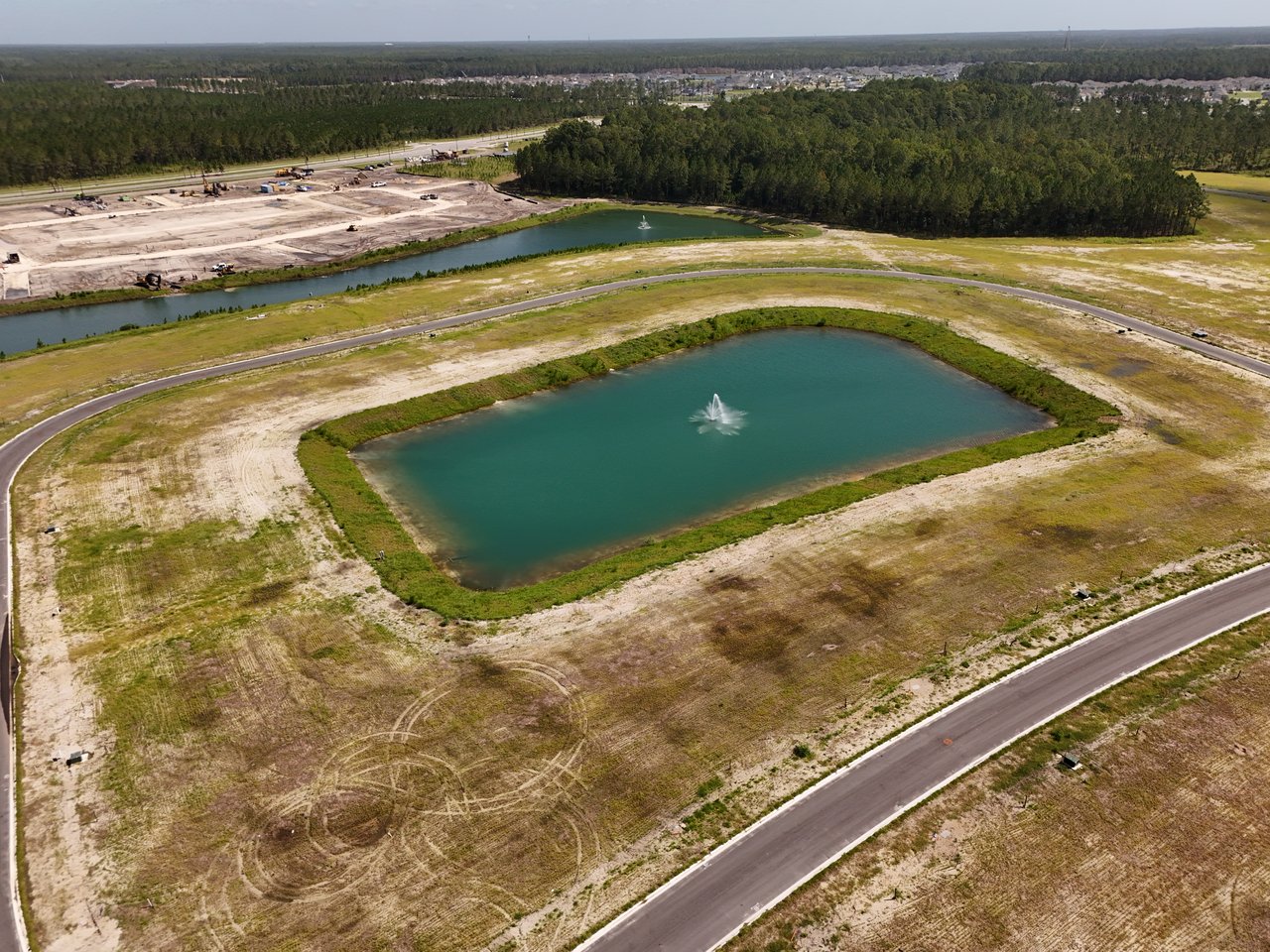 Aerial view of a developing community with a fountain pond, graded lots, roads, and woods.