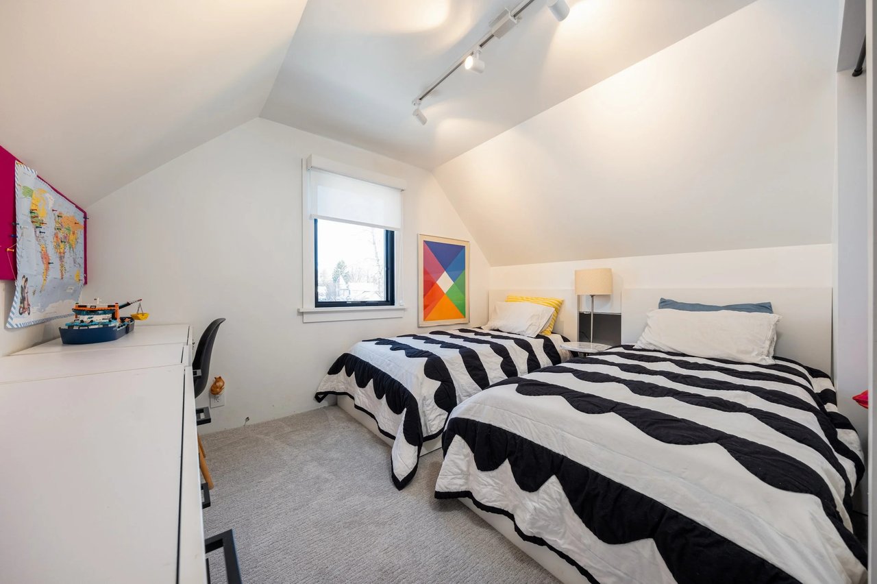 Attic bedroom with two twin beds in black-and-white striped quilts beneath a sloped ceiling.