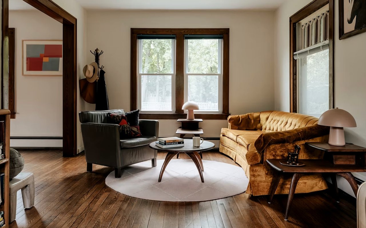 Living room with a caramel tufted sofa, black leather armchair, and tall wood-trimmed windows.