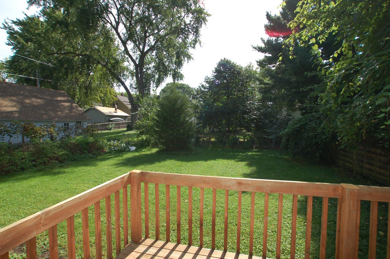Wooden deck overlooking a leafy backyard with a broad lawn and mature trees.