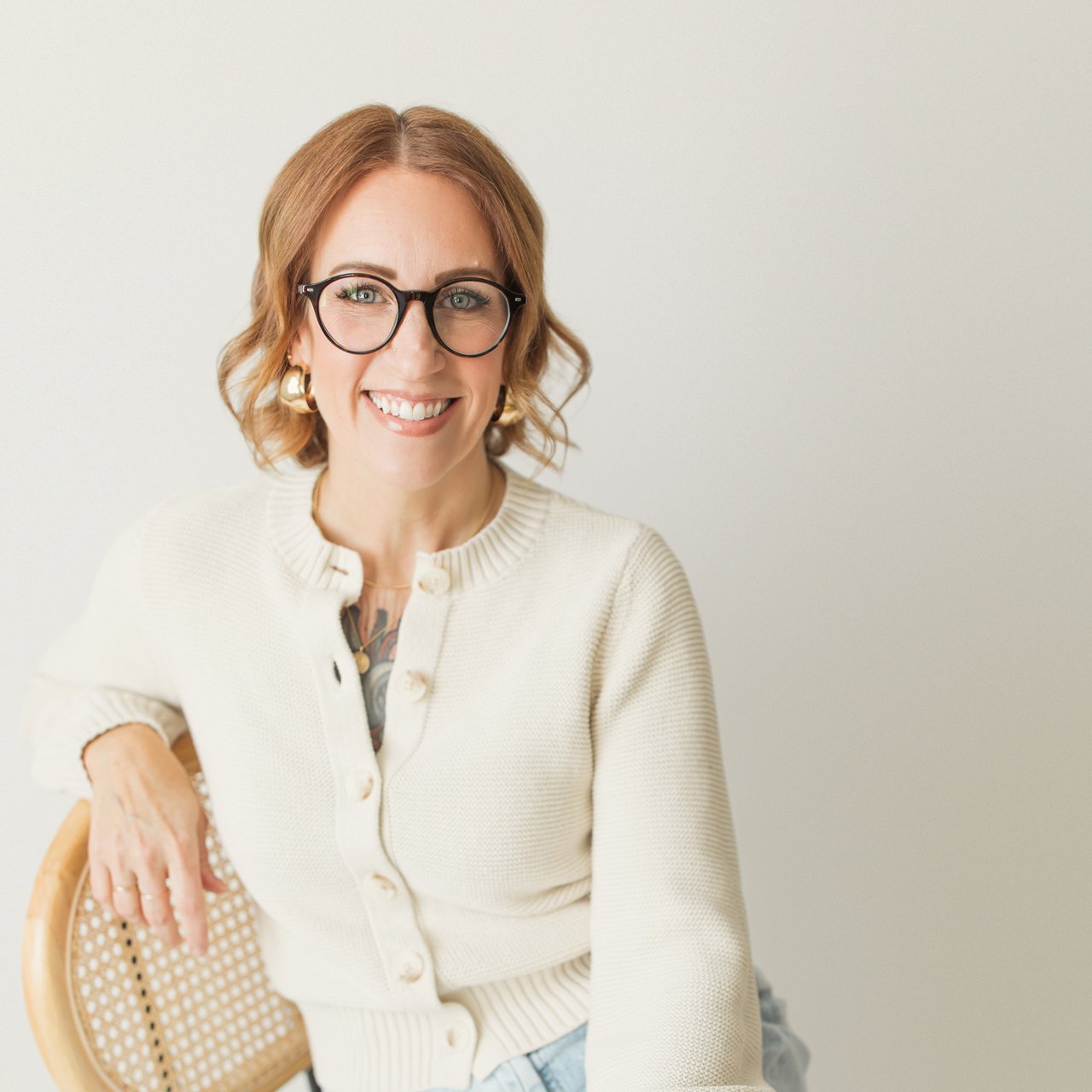 Jaclyn Broesel, a smiling real estate agent in black glasses and a cream cardigan.