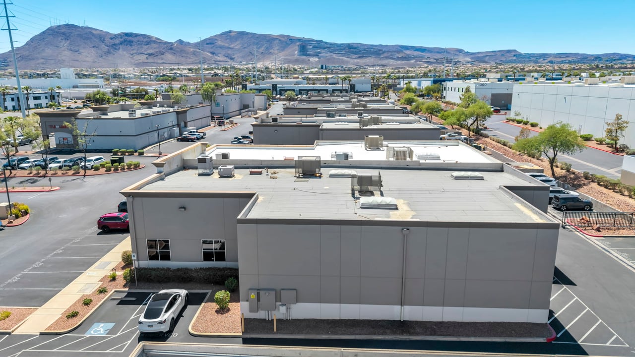 Commercial building with a broad flat roof, parking lots, and mountains in the distance.