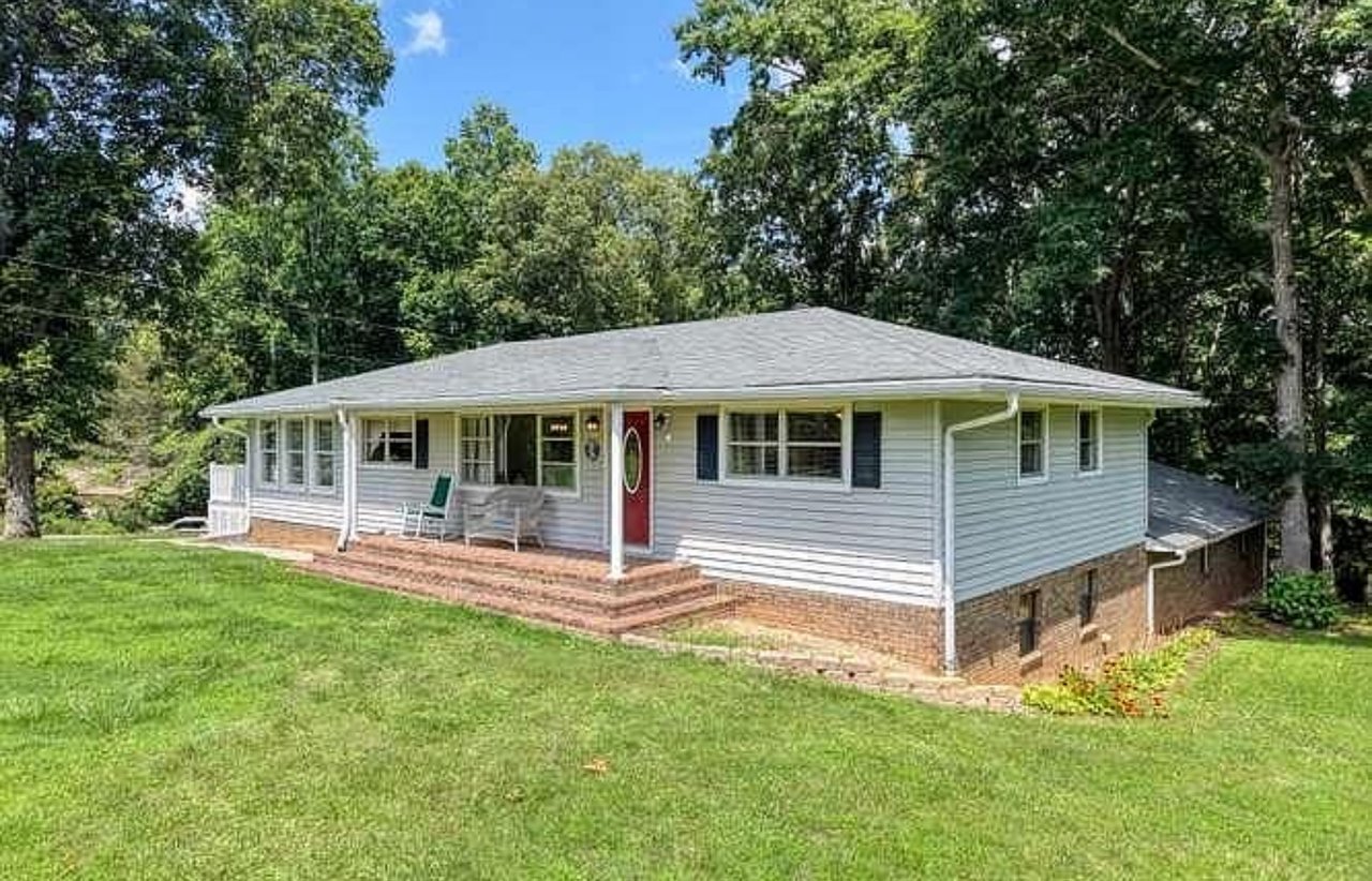 Single-story ranch house with a red front door, brick foundation, and a spacious lawn.