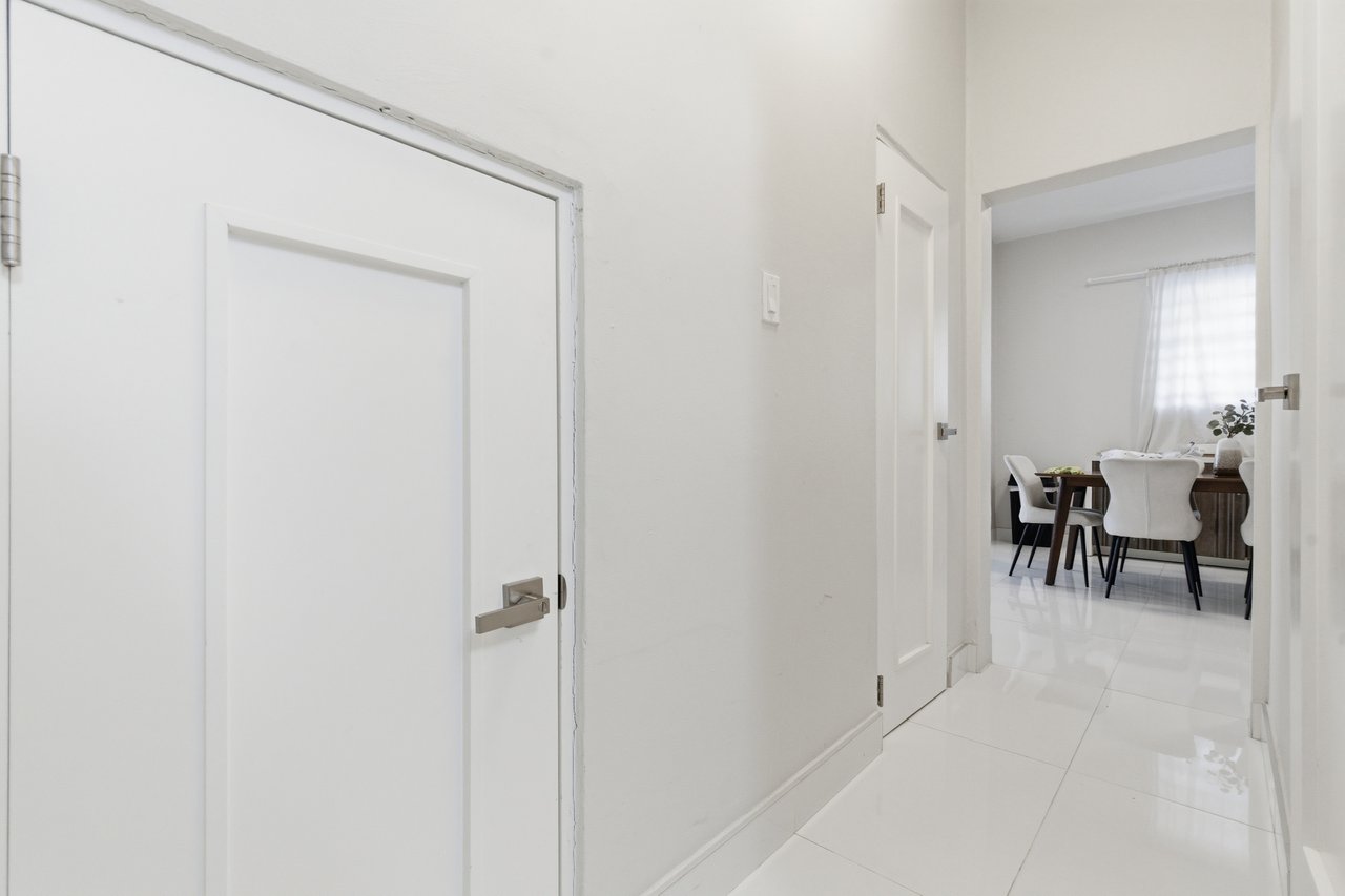 White-tiled hallway leading to a dining area with upholstered chairs.