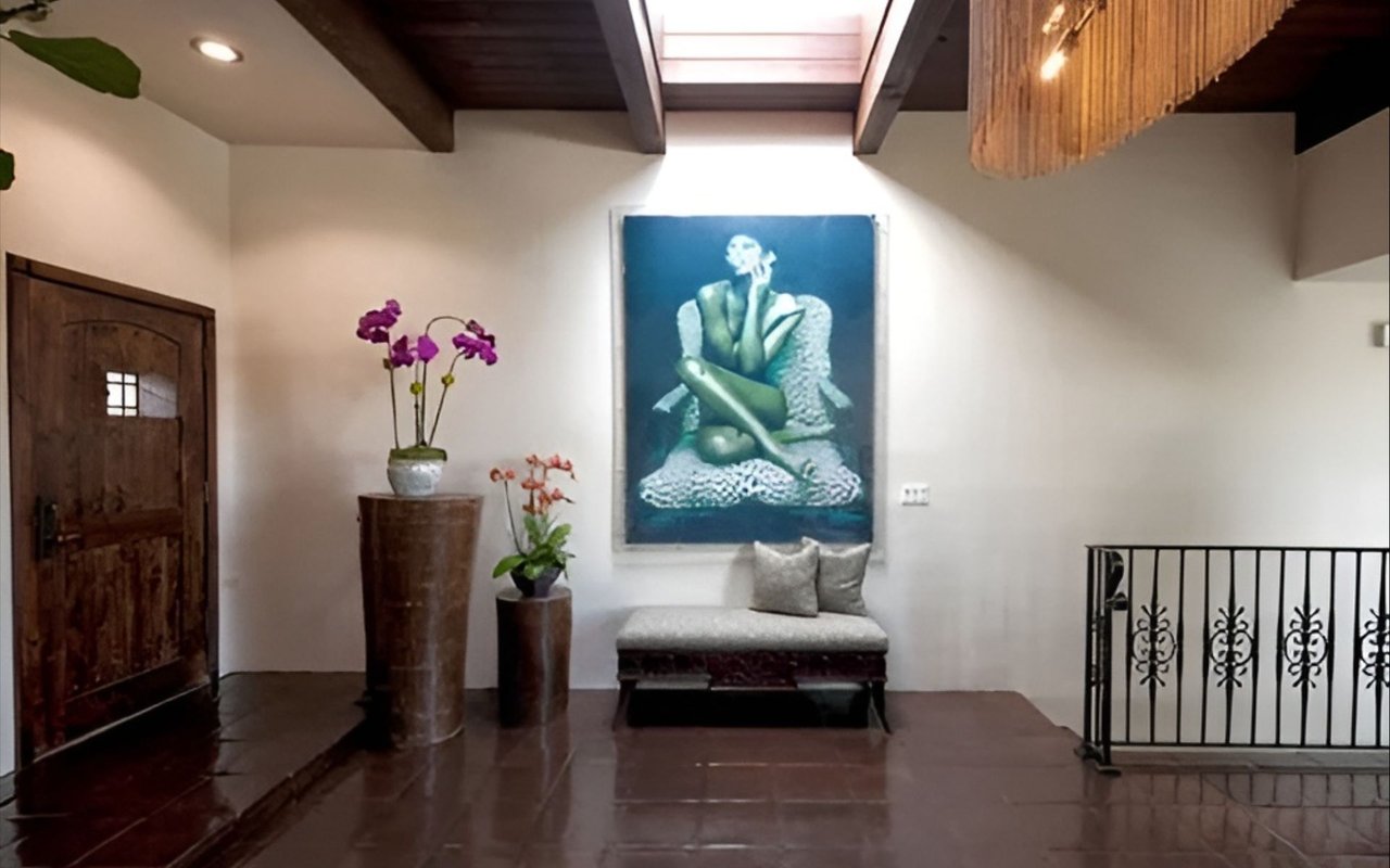 Entry hall with a dark wood door, orchid planters, and a bench beneath a large painting.