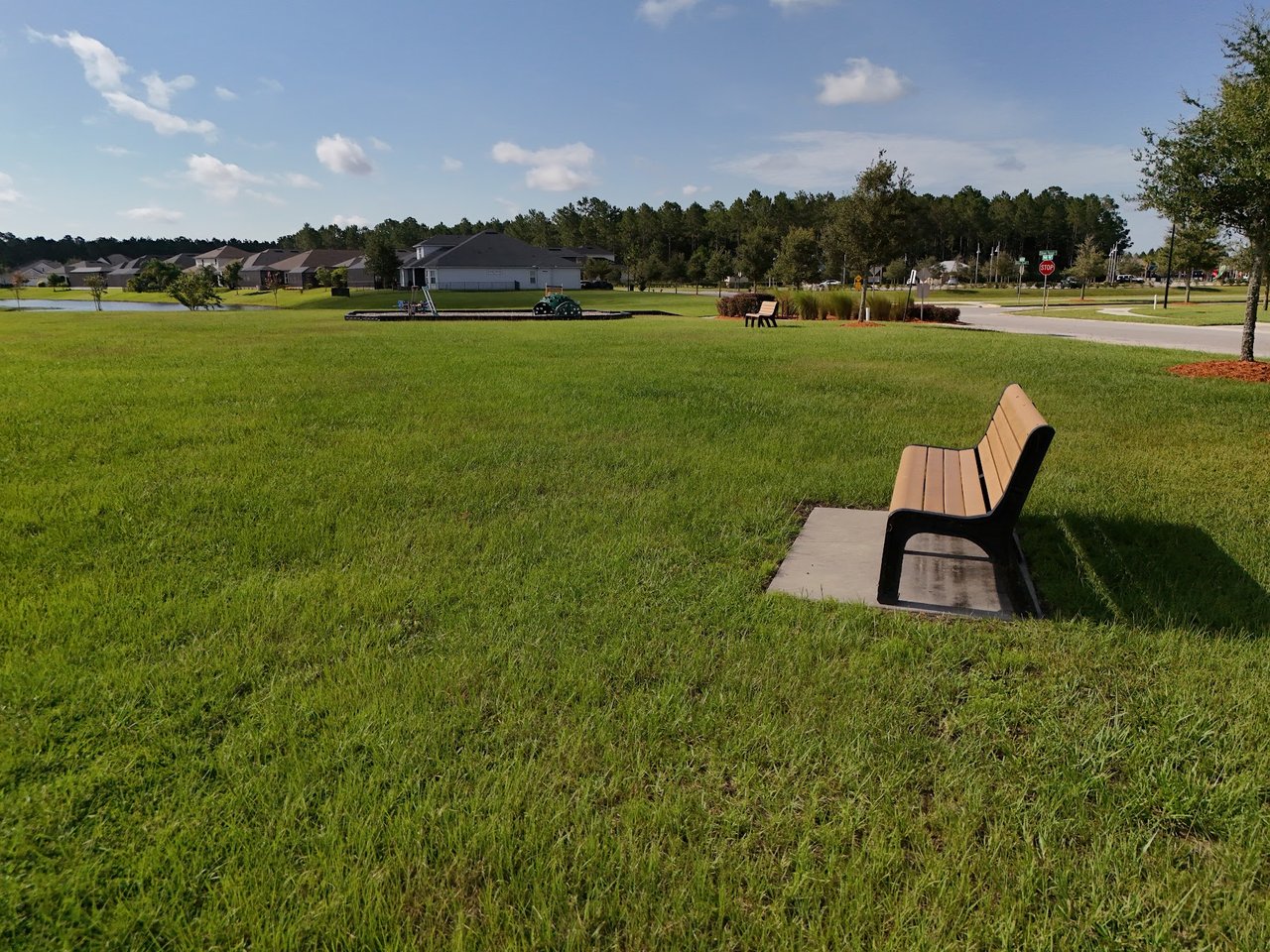 Neighborhood green space with a wooden bench, homes, and a stop sign in the distance.