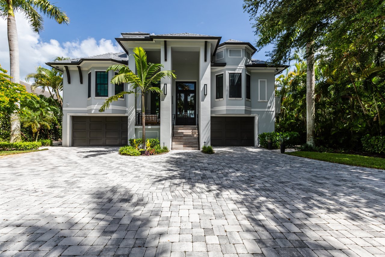 Modern two-story home with a central raised entry, twin garages, and a broad paver driveway.