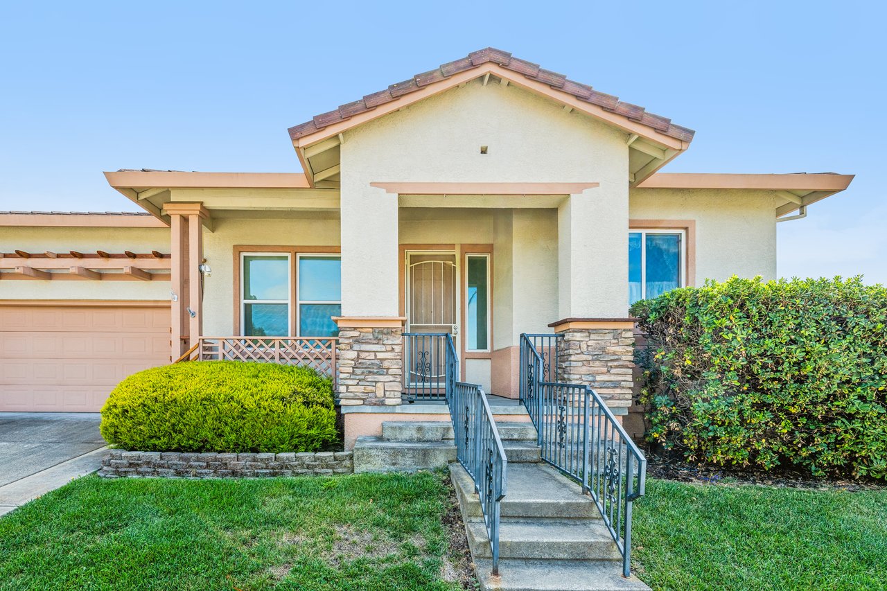 Single-story stucco home with stone porch pillars, a railed entry stair, and attached garage.