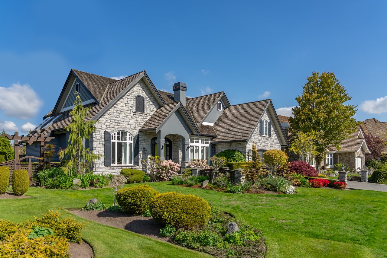 Stone-fronted home with multiple gables, a covered entrance, and landscaped gardens.