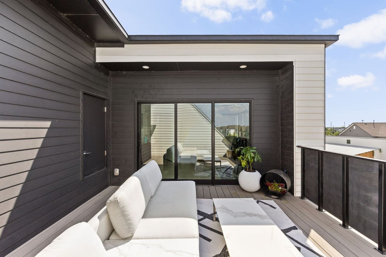 Rooftop deck with a white sectional, coffee table, potted plants, and sliding glass doors.