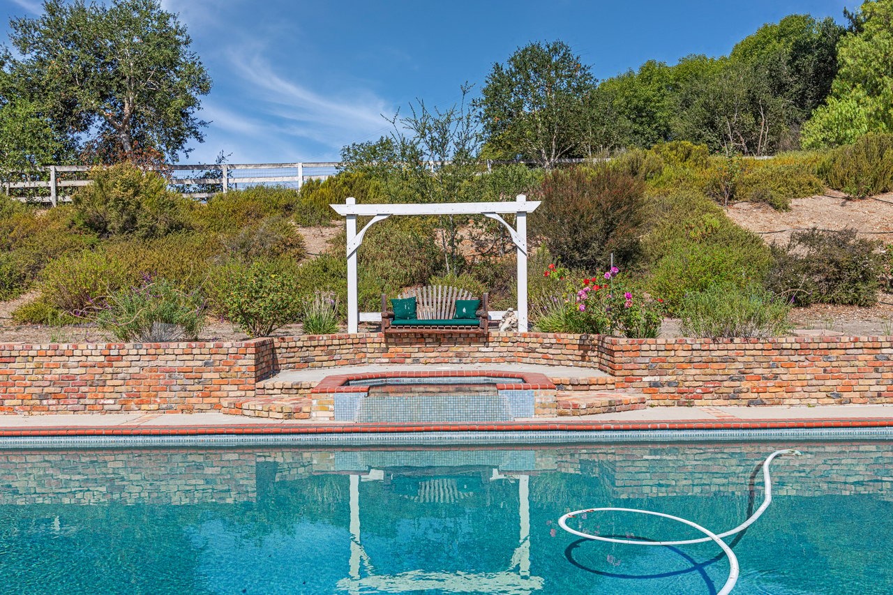 Swimming pool and raised spa below a pergola-shaded bench and landscaped hillside.