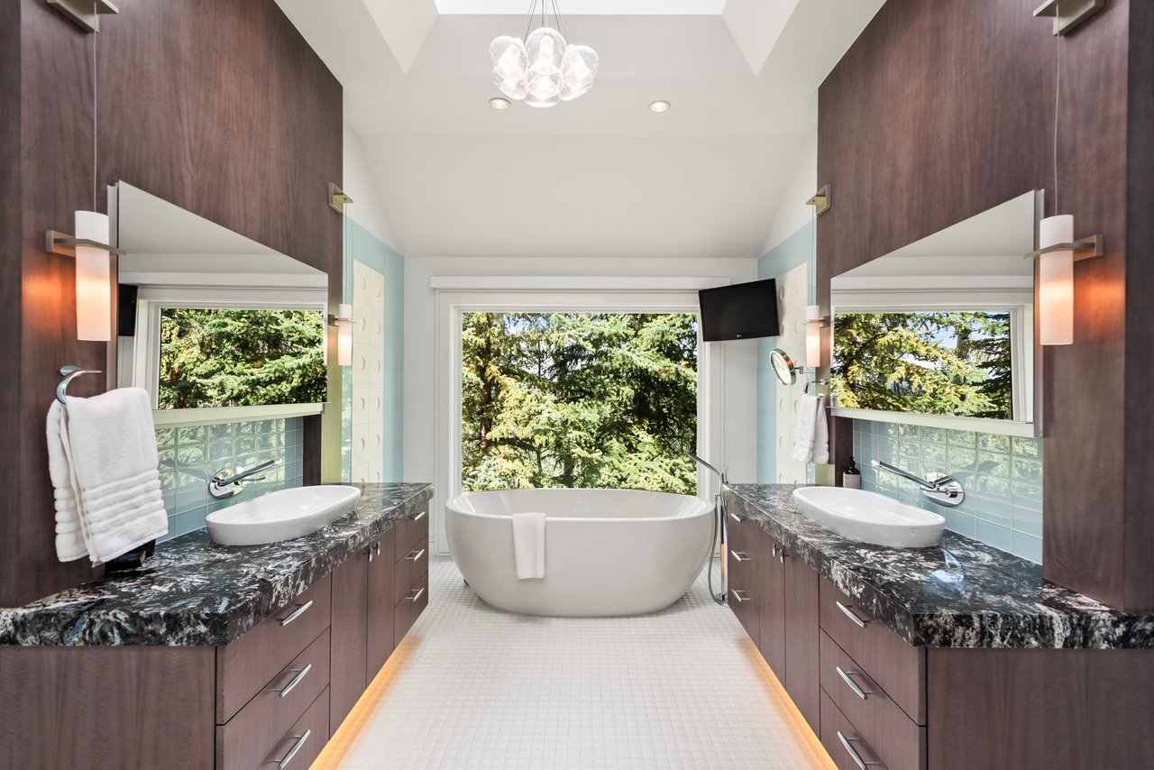 Bathroom with a freestanding soaking tub, tree views, and matching double vanities.