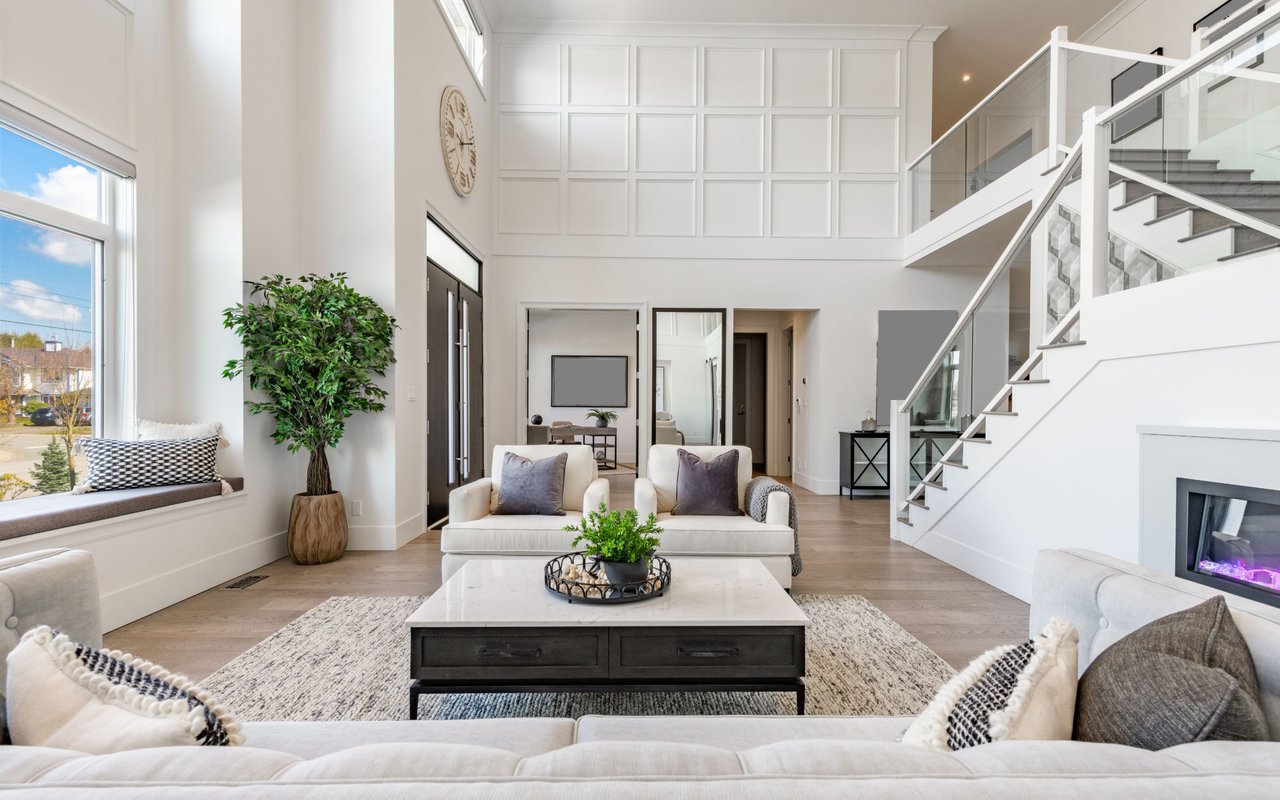 Bright living room with white sofas, a double-height paneled wall, and an open staircase.