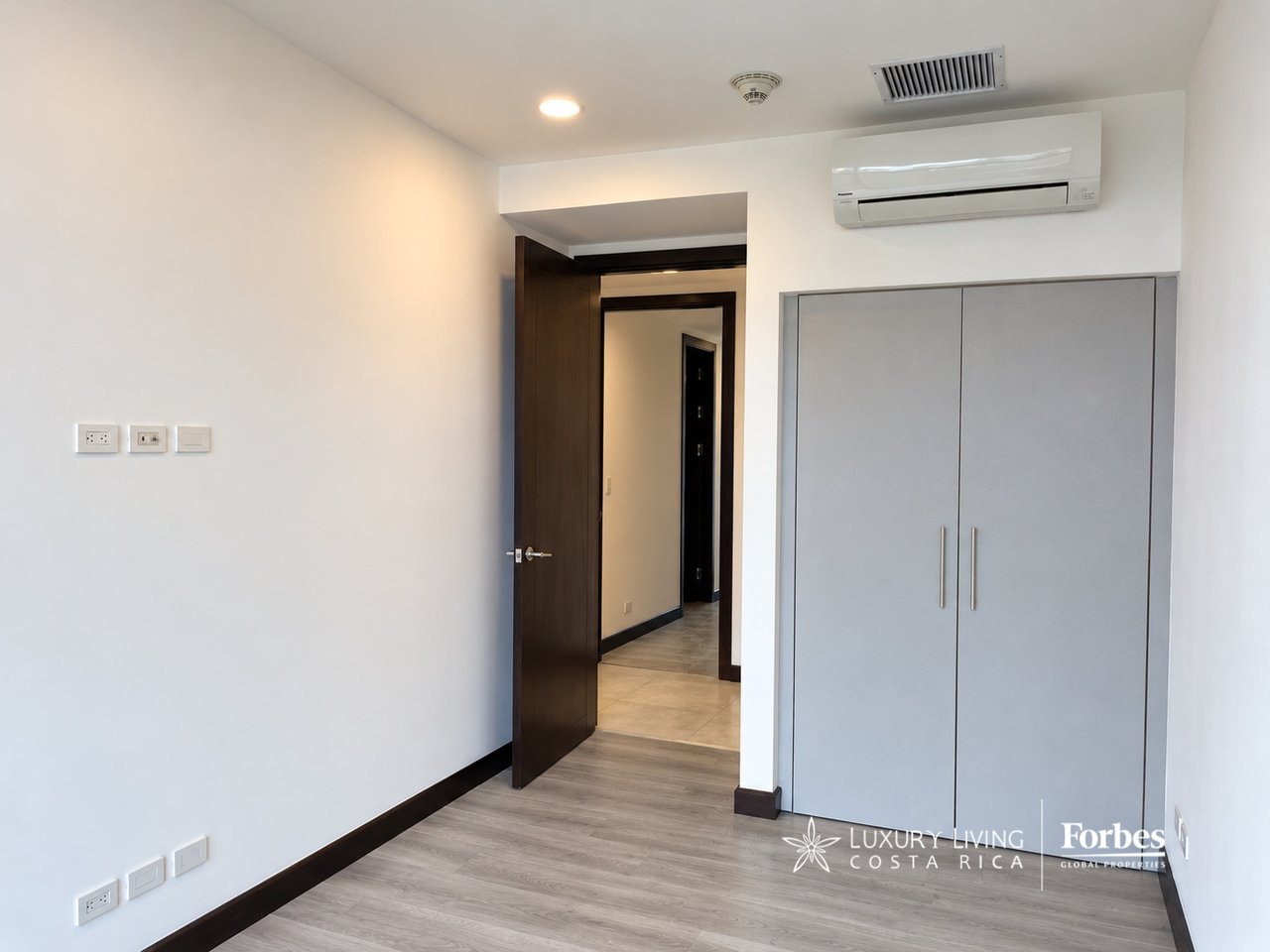 Empty apartment room with a built-in gray wardrobe, wood-look flooring, and an open doorway.