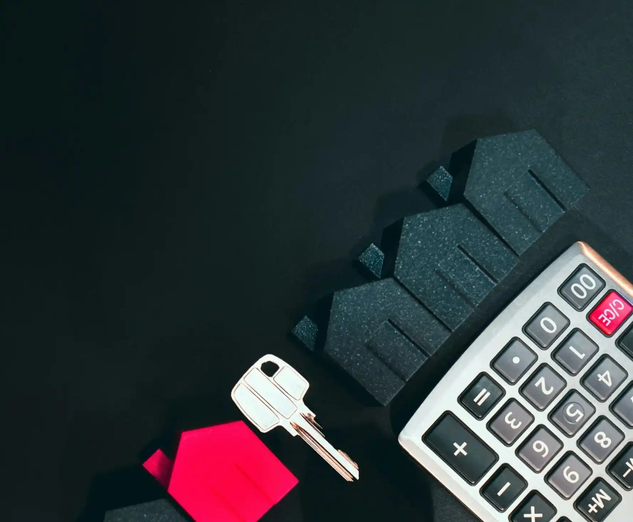 Calculator, house key, and small house models on a dark surface, symbolizing mortgage payments and home financing.