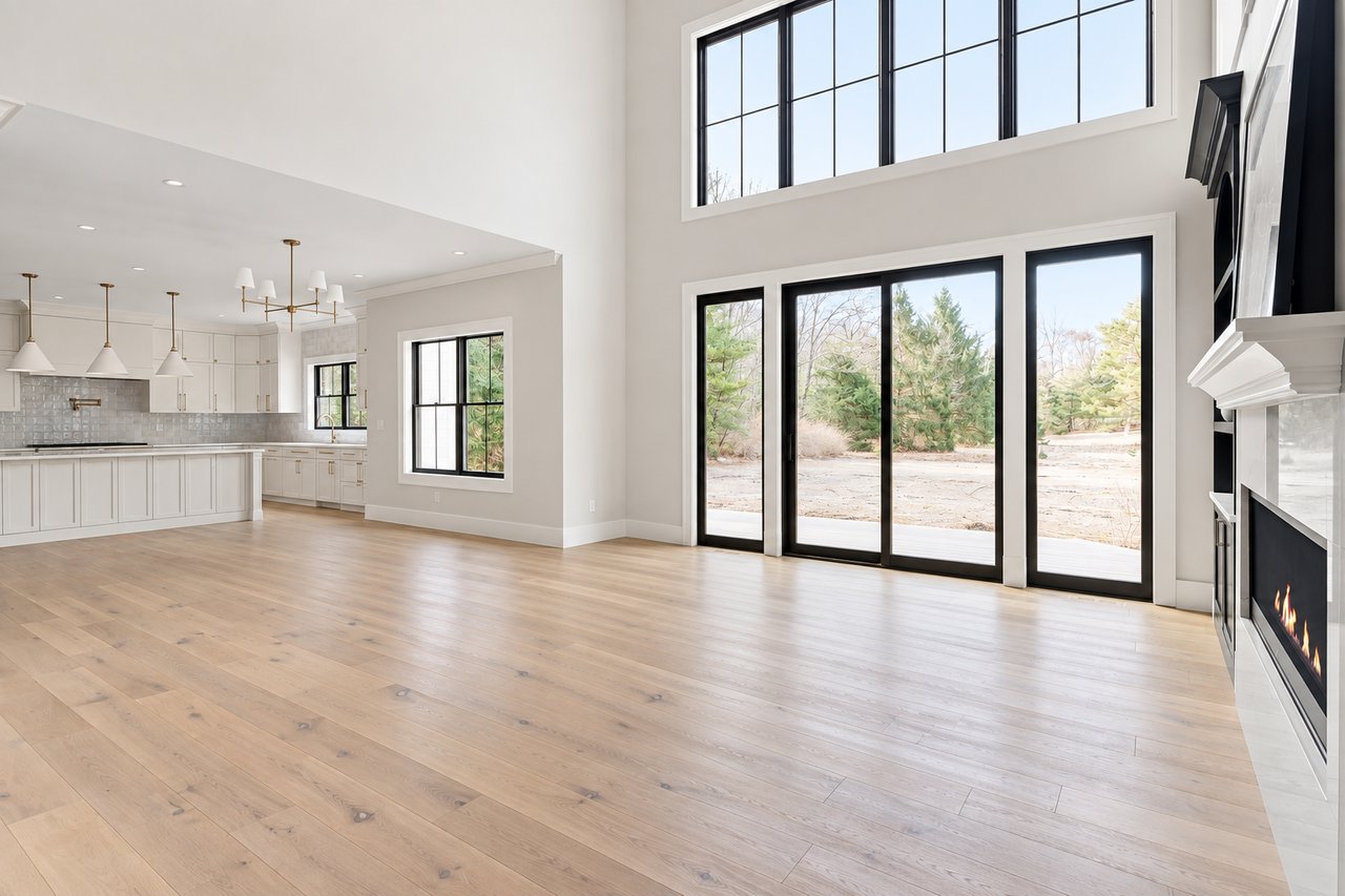 Open-plan living room and kitchen with tall windows, pale wood floors, and a modern fireplace.