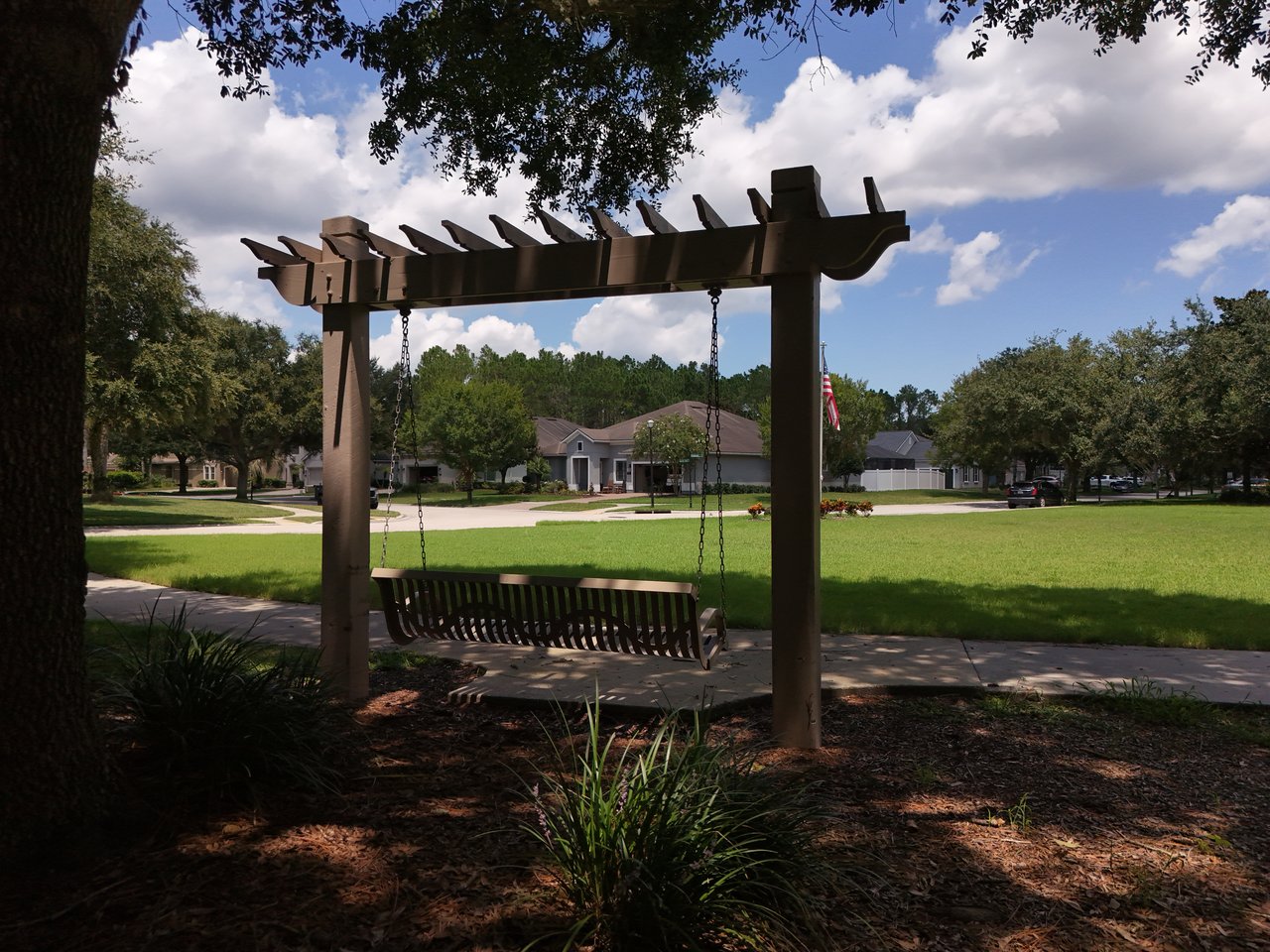 Neighborhood park with a wooden pergola swing, lawn, and homes across the street.