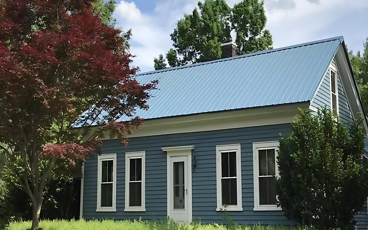 Blue-sided historic-style house with white trim and a standing-seam metal roof, framed by trees.