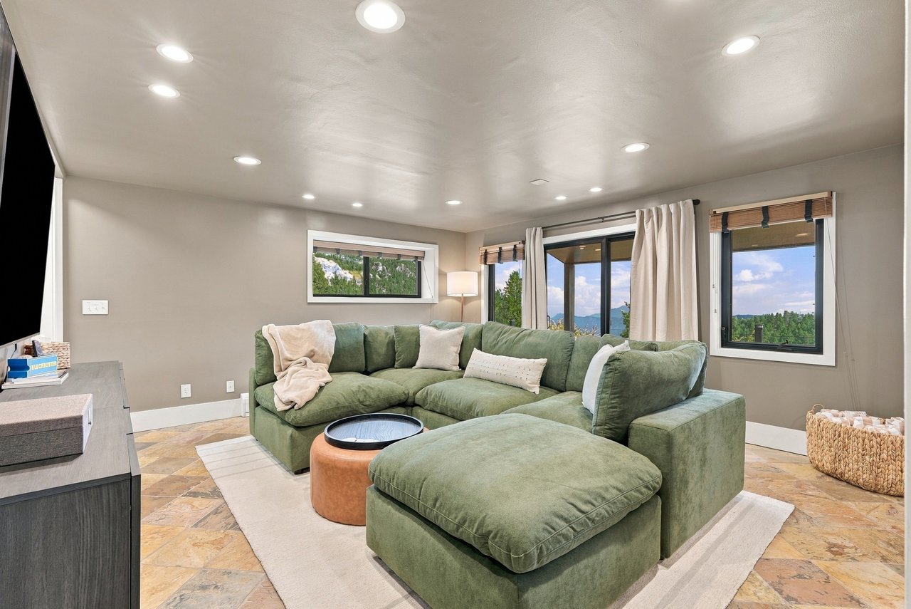 Living room with a green sectional sofa and windows overlooking trees and distant mountains.