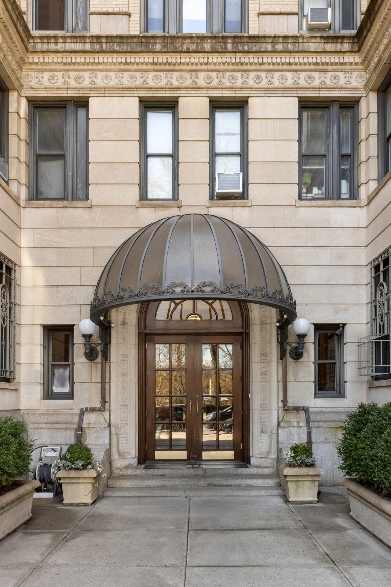 Symmetrical entrance of a beige stone building featuring double wooden doors under a rounded glass and metal awning.