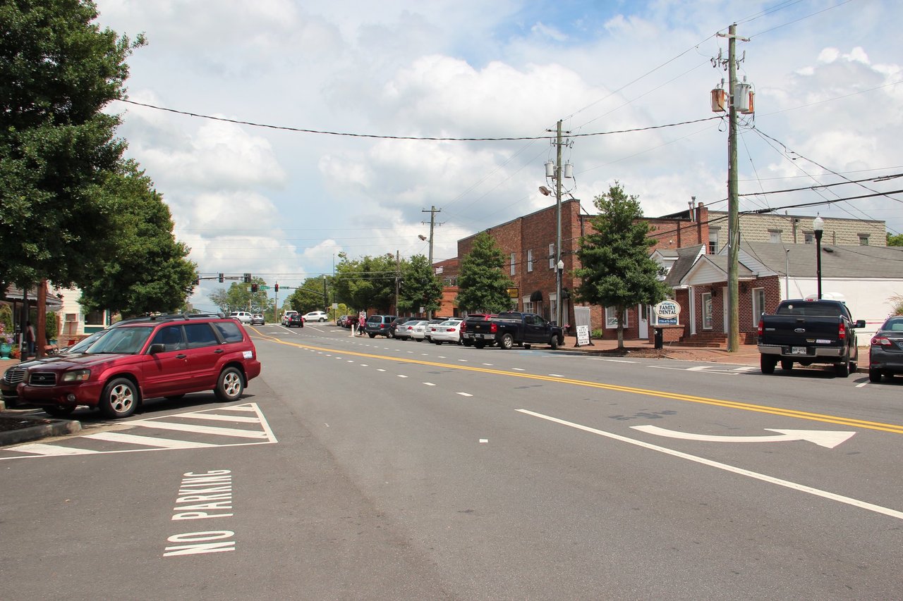 Street in downtown Alpharetta, Georgia with brick storefronts, trees and parked cars on a sunny day
