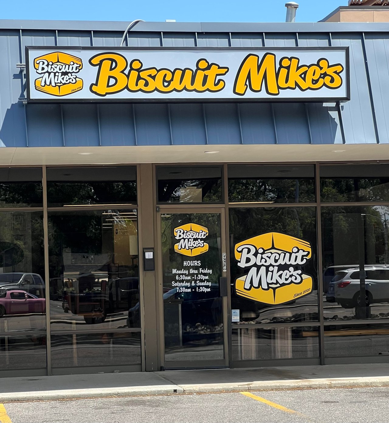 Biscuit Mike's storefront with prominent yellow signage and hours posted on the glass entrance.