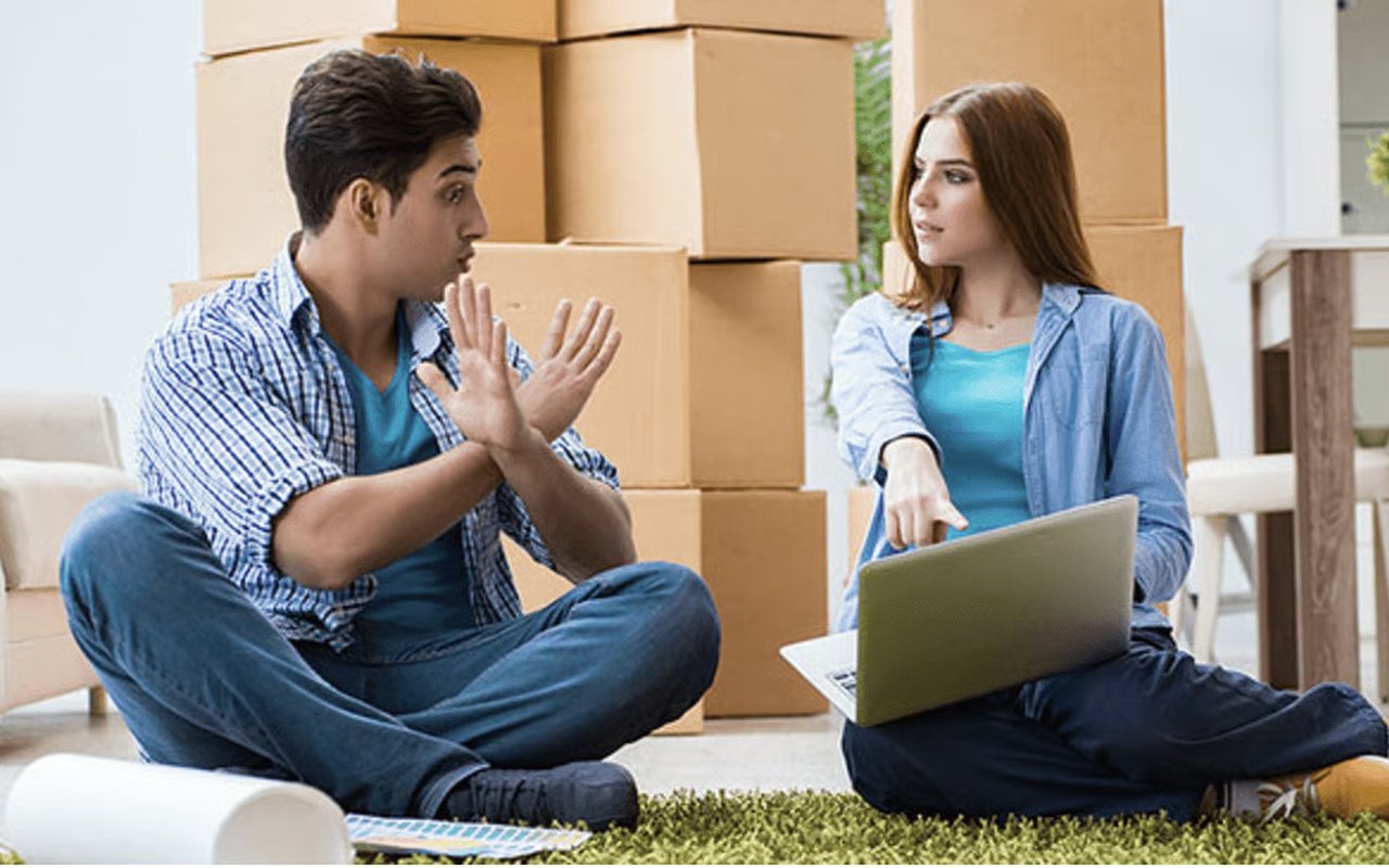 A couple discusses a move among packed boxes, with the woman pointing at a laptop.