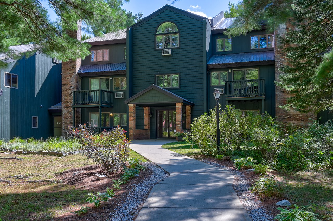 River Run condominium building with teal siding, brick accents, balconies, and a landscaped entrance walkway.
