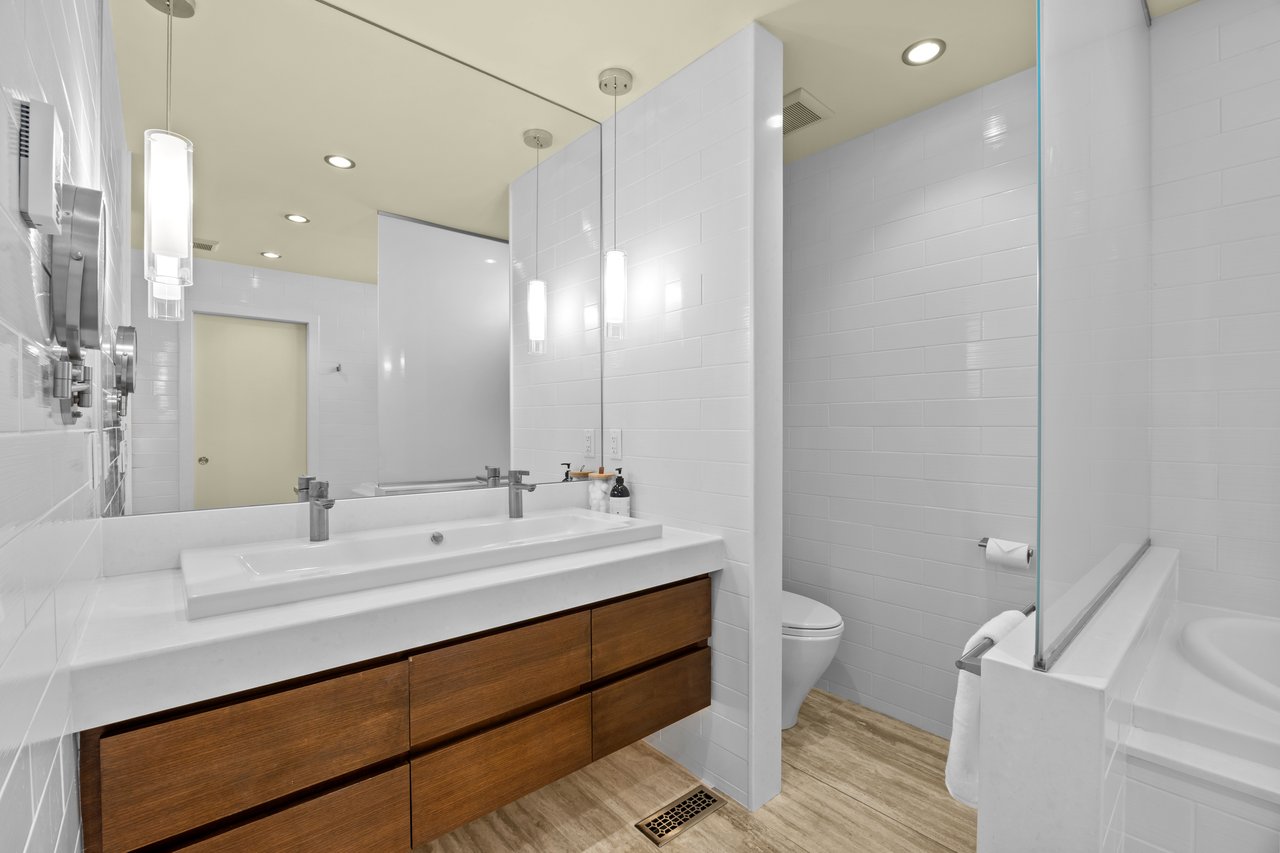 Modern bathroom with a long wood vanity, double sinks, and glass-enclosed tub and shower.